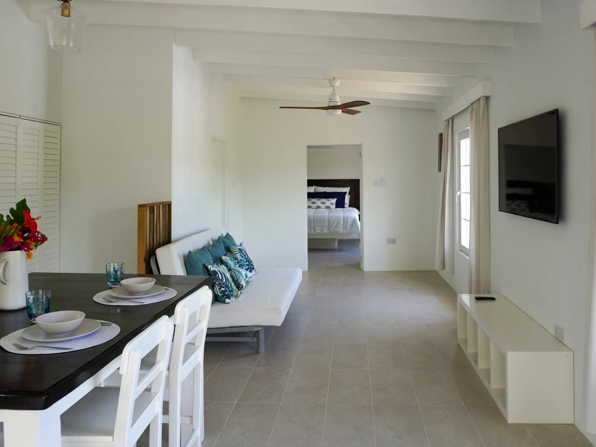 Living area looking through to the bedroom, with TV and ceiling fan